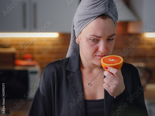 Sick woman trying to sense smell of fresh orange, has symptoms of Covid-19, corona virus infection. Long-lasting covid19 symptom. Loss of taste of food. Loss of smell as one of long-term sars-cov-2 photo