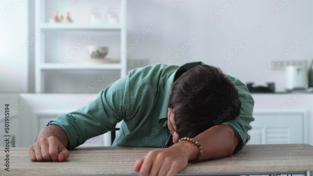 Portrait of worried and stressed young man sitting at table at home. Depressed male suffering from grief or failure Portrait of worried and stressed young man sitting at table at home. Depressed male suffering from grief or failure