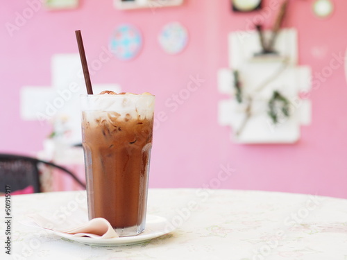 Ice coffee in a tall glass with cream poured over and coffee beans.
