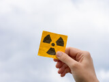 A woman holding a radiation warning sign in her hand against an overcast sky background