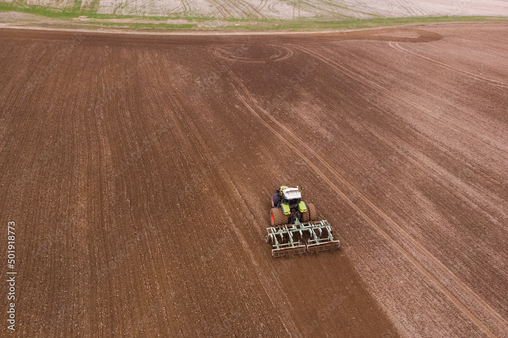 A tractor with a disc harrow plows a field for sowing crops. Aerial photography.