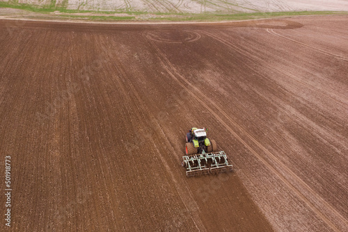 A tractor with a disc harrow plows a field for sowing crops. Aerial photography.