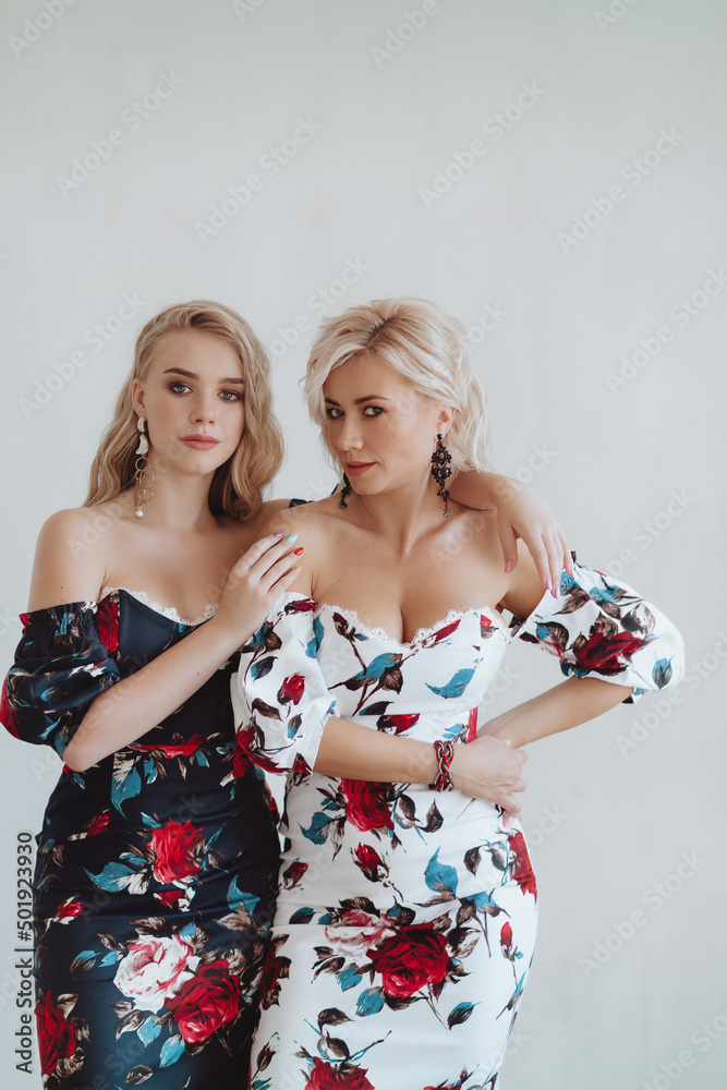 Beautiful young mother and her teenage daughter in identical dresses with roses on a light background. Teen parenting concept Beautiful young mother and her teenage daughter in identical dresses with roses on a light background. Teen parenting concept