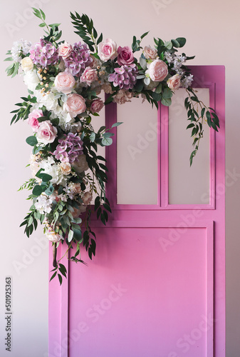 Pink wooden doors in vintage style, surrounded on one side by pink roses, peonies, various flowers. With space to copy. High quality photo