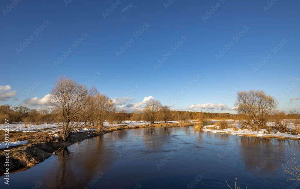 March sunny day by the river. A picturesque landscape, early spring, a river with snow-covered banks. The first thaws, the snow is melting.