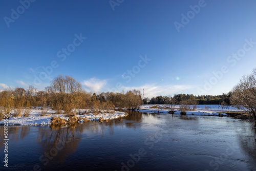 March sunny day by the river. A picturesque landscape, early spring, a river with snow-covered banks. The first thaws, the snow is melting. © Sergei