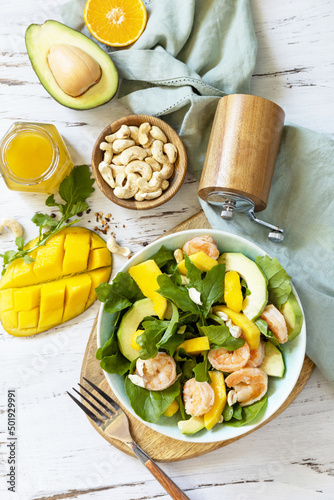 Vegetarian vegan healthy food. Salad with arugula, mango, avocado, shrimp, pecans and dressing of olive oil, honey and wine vinegar on a white rustic kitchen table. Top view, flat lay background.