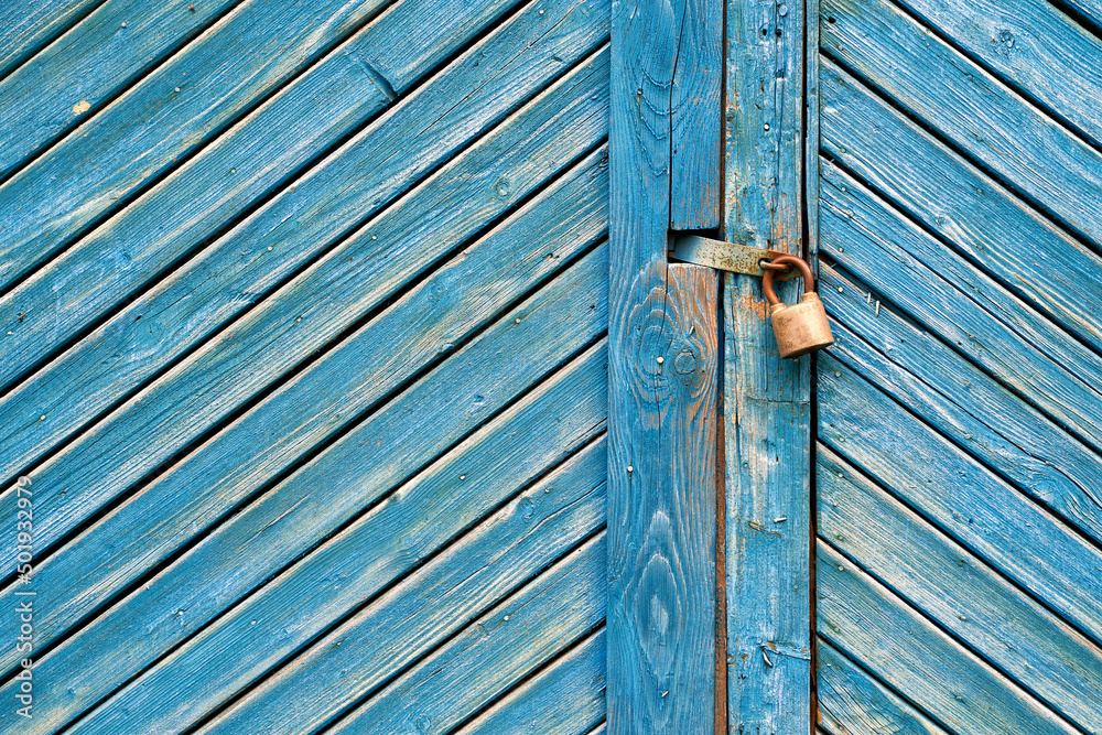Old padlock on a weathered retro blue wooden door. Textured background.