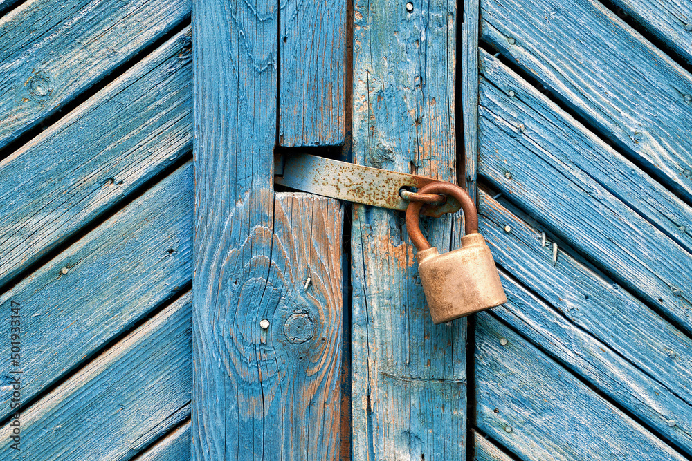 Closeup of old padlock on a weathered retro blue wooden door. Textured background.