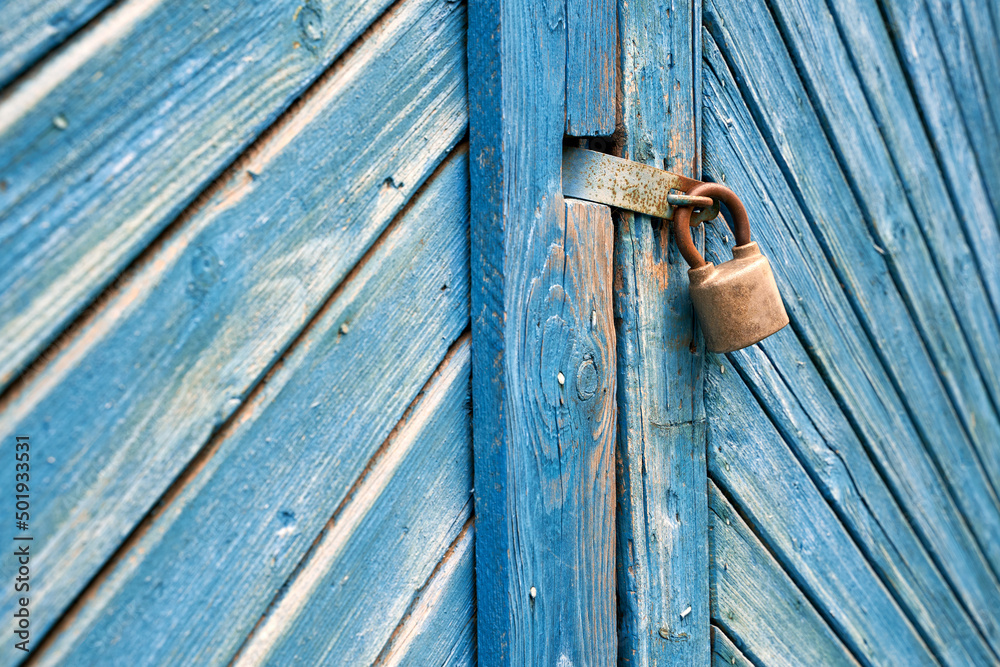 Old padlock on a weathered retro blue wooden door. Textured background.