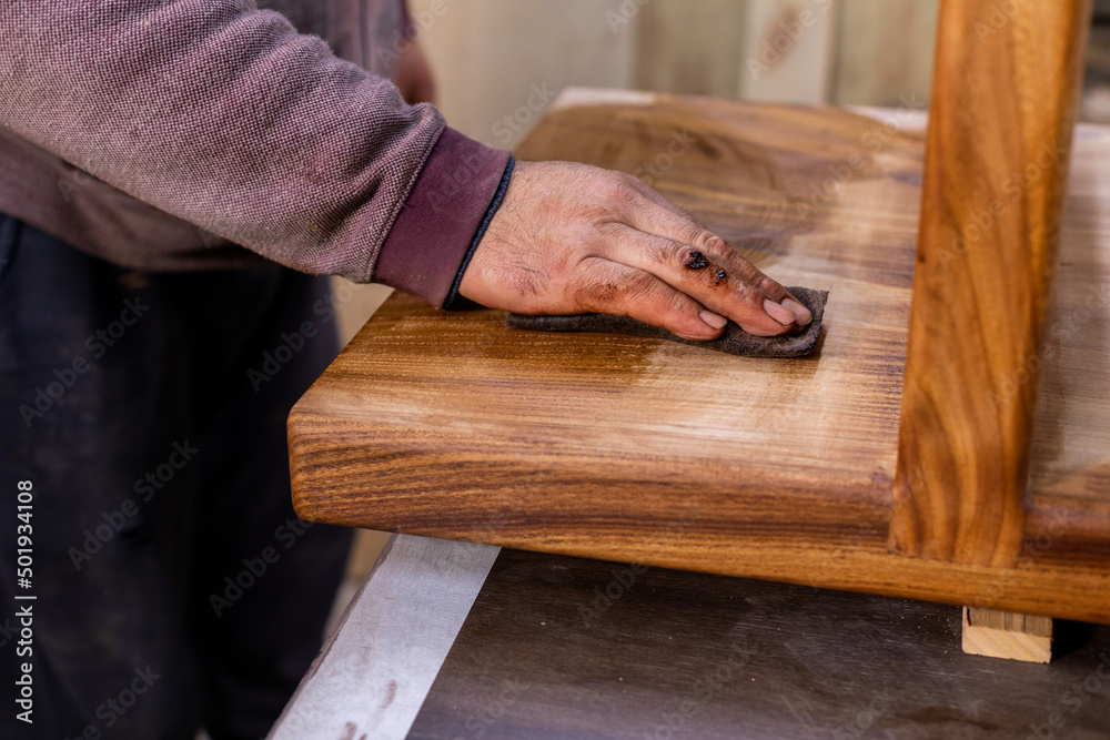 Closeup of carpenter coating a wooden table with protective flaxseed oil Closeup of carpenter coating a wooden table with protective flaxseed oil