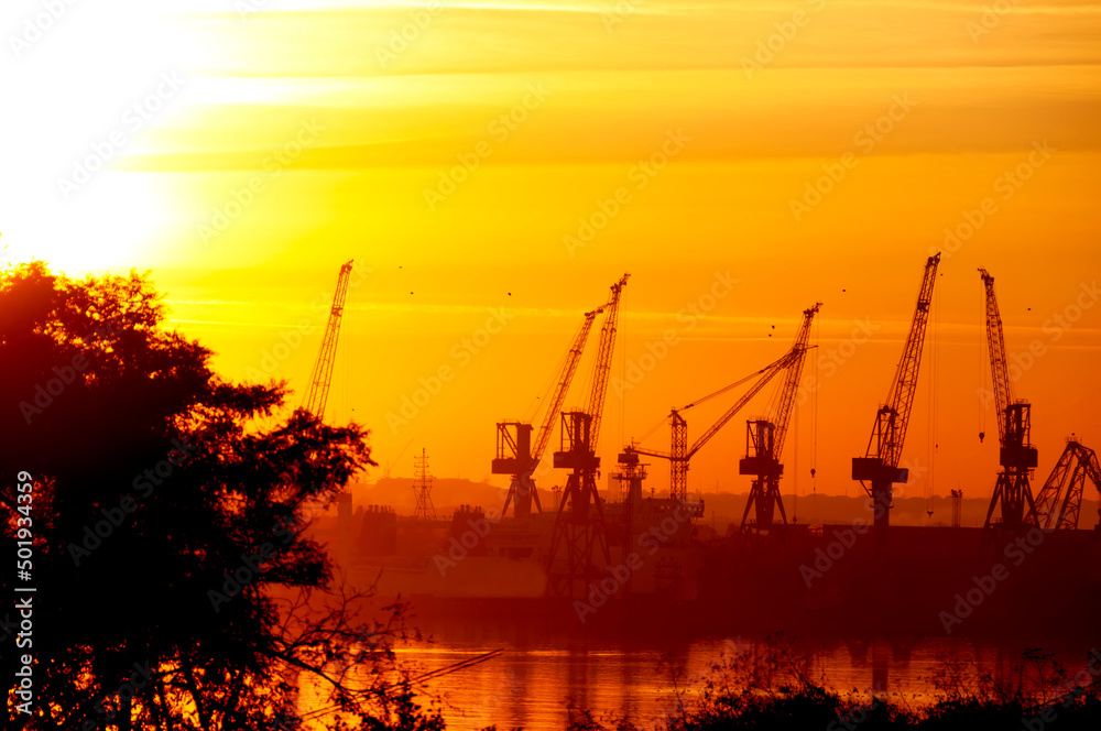 Silhouettes of port cranes on the seashore and against the backdrop of a magnificent sunset sky. Ukraine. Odessa region. Chernomorsk. Black Sea.