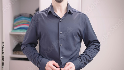 Headless muscular man dressing up elegant blue shirt in bedroom