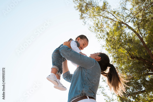 young mother lifts her son in her arms in the park at sunset - low angle