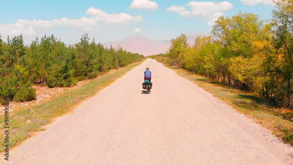 Tracking back view male cyclist cycling on middle of asphalt road alone outdoors with mountain panorama. Adventure travel outdoors background concept Tracking back view male cyclist cycling on middle of asphalt road alone outdoors with mountain panorama. Adventure travel outdoors background concept
