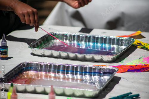 Colorful Oil Dipped Painting in a Tray of Water with a Hand Designing a Pattern in the Paint