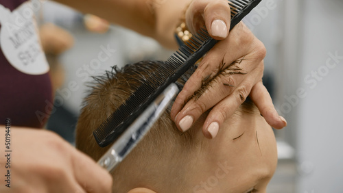 Process of hairdresser cutting hair. Blond caucasian boy is sitting in barber shop and hairdresser girl is cutting his hair. Child gets fashionable haircut, hairdresser cuts child hair with scissors.