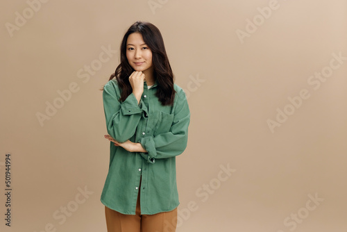 Korean beauty. Happy cheerful Asian student young woman in khaki green shirt recline on hand posing isolated on over beige pastel studio background. Cool fashion offer. Lifestyle and Emotions concept