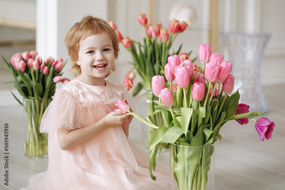 Child girl in a pink dress among tulips in vases Child girl in a pink dress among tulips in vases