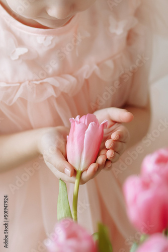 Child girl in a pink dress holds a tulip bud in her hands