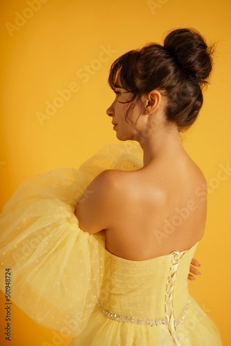 Profile portrait of a beautiful middle-aged woman in a yellow dress, her hair pulled up against a yellow background