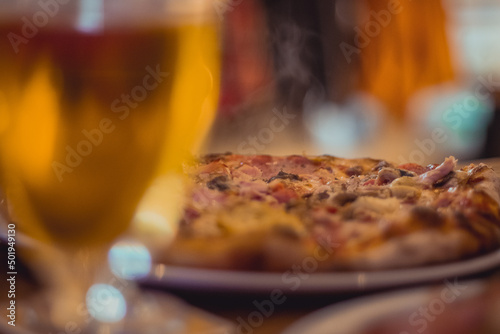 Fresh pizza served on a plate with some vapor rising up, surrounded by glasses of beer. Tasty and delicious oven pizza.