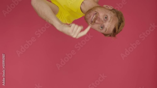 Follow me - Vertical shot view of excited young adult man in yellow shirt stretching arm to camera inviting to follow him - Come here concept with cheerful guy inviting approach over red background photo