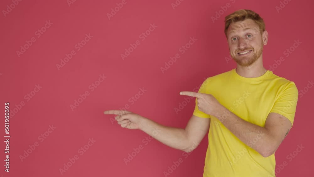 Smiling young adult man in yellow shirt pointing with fingers over isolated red background studio. Cheerful hispanic latino male showing copy space to the side Smiling young adult man in yellow shirt pointing with fingers over isolated red background studio. Cheerful hispanic latino male showing copy space to the side