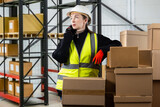 Warehouse manager with phone. Girl in reflective vest calls client. Woman manager of warehouse company. Woman in white paint in front of cardboard boxes. Logistics warehouse manager career