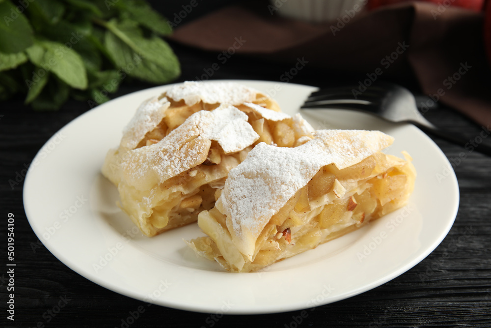 Delicious apple strudel with almonds and powdered sugar on black wooden table, closeup Delicious apple strudel with almonds and powdered sugar on black wooden table, closeup