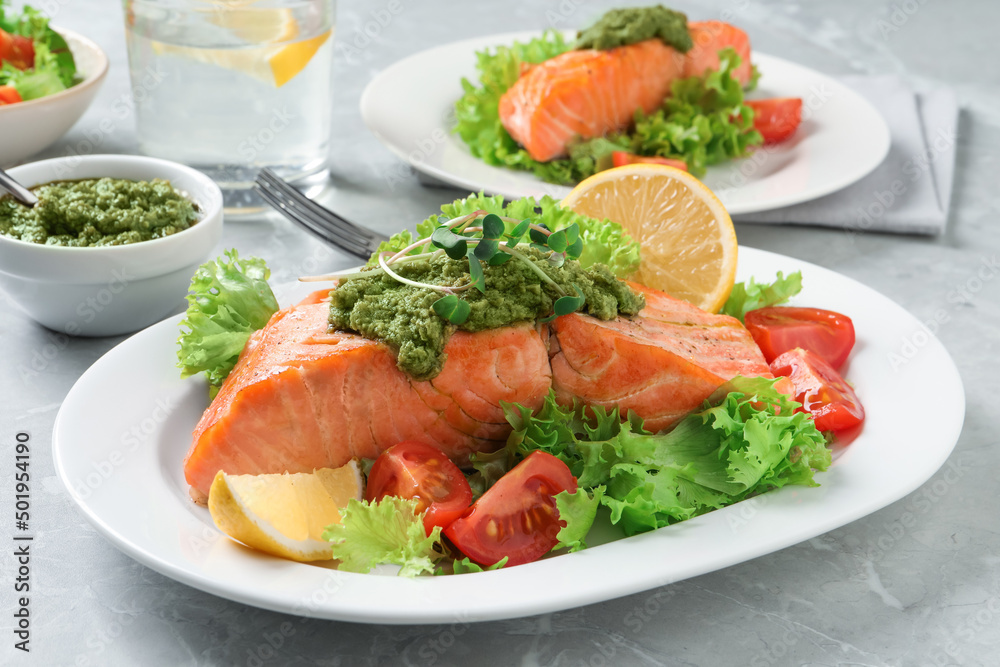 Tasty cooked salmon with pesto sauce and fresh salad served on grey table