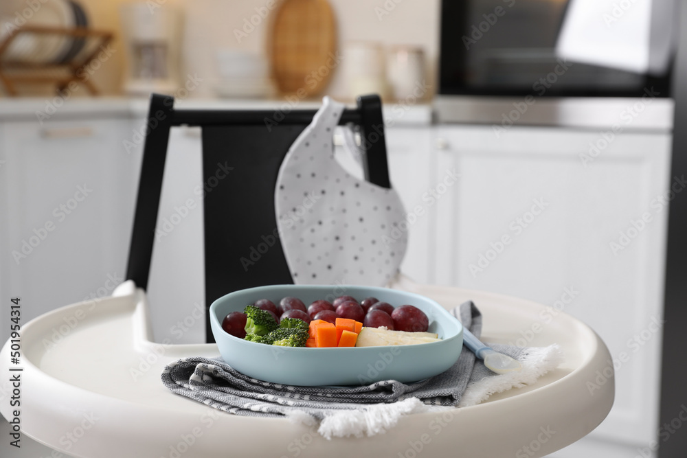 High chair with food in baby tableware on tray indoors High chair with food in baby tableware on tray indoors