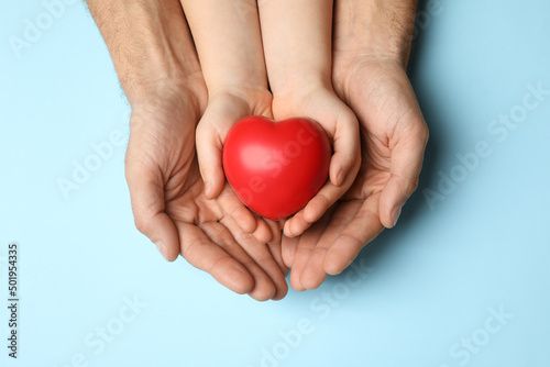 Man and kid holding red heart in hands on light blue background  top view