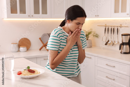 Young woman feeling nausea while seeing food at table in kitchen