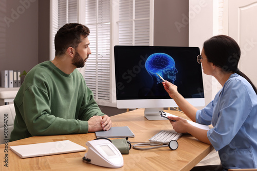 Neurologist showing brain scan to sad man in clinic photo