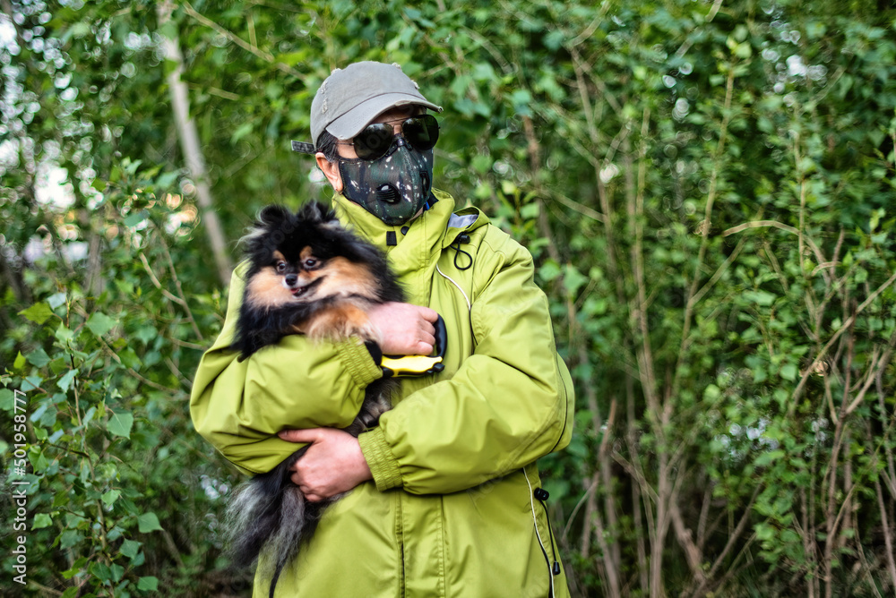 Obraz premium A girl wearing respirator mask walking with a Pomeranian dog in the forest protecting from COVID-19.