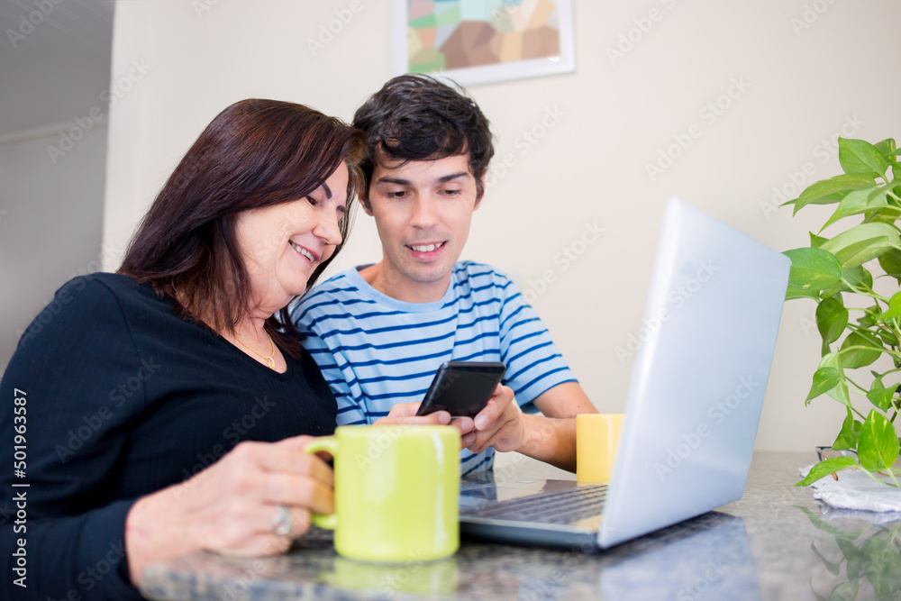 Happy mother and son together using a mobile app to order or shop online. Family shopping online through mobile app or computer. On the wall, digitally created mosaics to simulate two paintings. Happy mother and son together using a mobile app to order or shop online. Family shopping online through mobile app or computer. On the wall, digitally created mosaics to simulate two paintings.