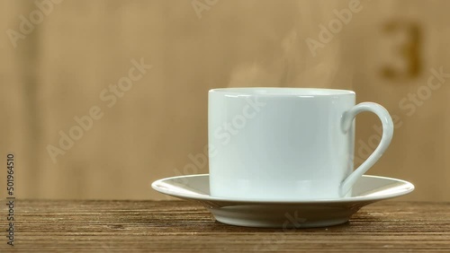 White coffee cup, hot coffee, smoke rising from the coffee cup on a wooden table on old cement wall background.