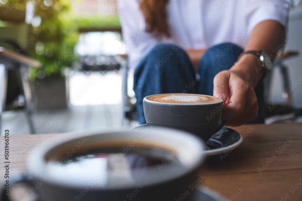 Closeup image of a young woman holding and drinking coffee with friend in cafe Closeup image of a young woman holding and drinking coffee with friend in cafe