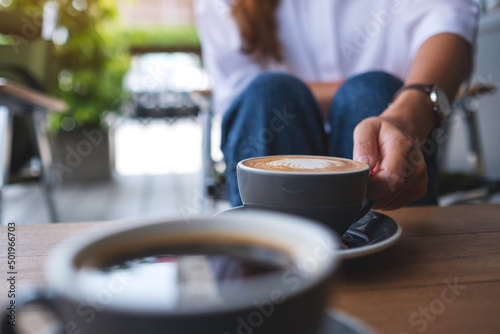 Closeup image of a young woman holding and drinking coffee with friend in cafe