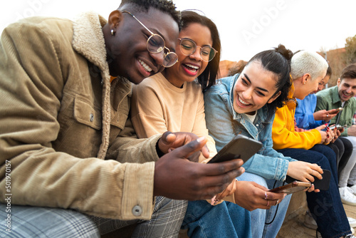 Happy multiracial teen college students having fun using mobile phone together in campus outdoors. photo