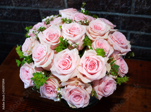Light pink roses in a bouquet on a table against a background of dark bricks.