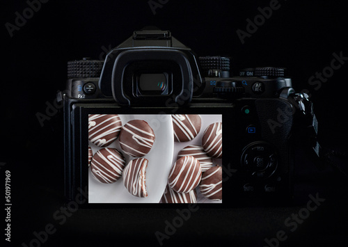 DSLR camera or mirrorless body lit by a rim light showing mint chocolates on the back of the camera display. Low key light photography photo