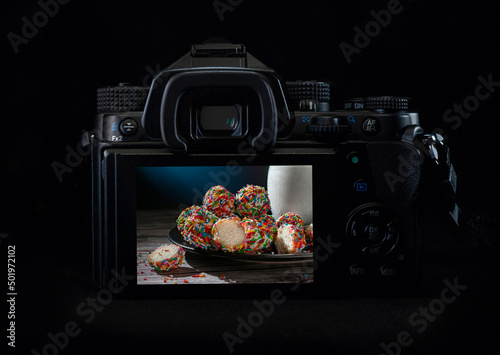 DSLR camera or mirrorless body lit by a rim light showing sweet bread and milk on the back of the camera display. Low key light photography photo