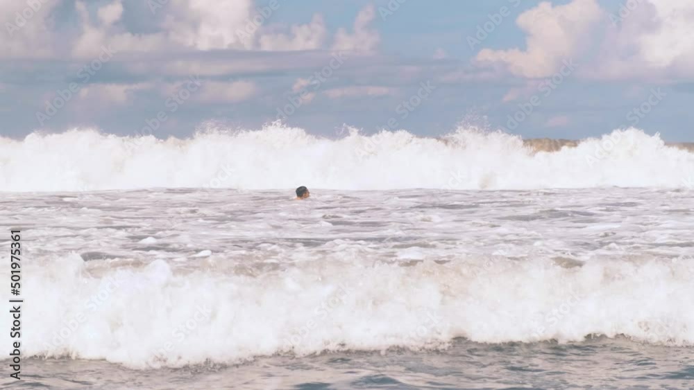 Athletic man swimming in the raging Indian Ocean off the coast of Bali in Indonesia, large surfing waves with white foam approaching the camera. Extreme leisure. Athletic man swimming in the raging Indian Ocean off the coast of Bali in Indonesia, large surfing waves with white foam approaching the camera. Extreme leisure.