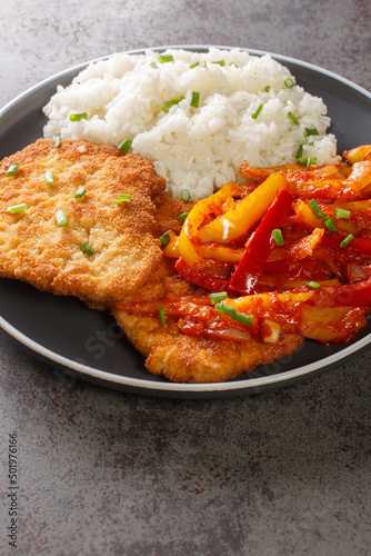German schnitzel served with paprika sauce and rice close-up in a plate on the table. vertical