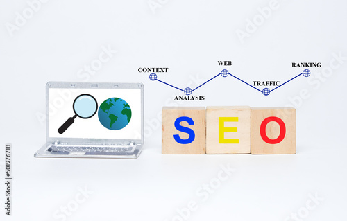 A picture of miniature laptop with magnifying and earth insight. SEO on wooden block. Context  analysis  web  traffic and ranking. Search Engine Optimization concept.