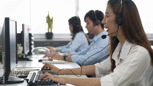 Call center young employee working with headset, Smiling customer support operator team at work surrounded by colleagues working in the office, Helpdesk customer services support agent concept