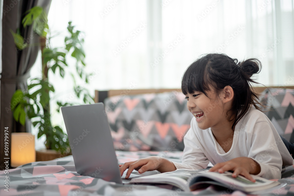 Little Asian girl using a laptop while lying on the bed Little Asian girl using a laptop while lying on the bed