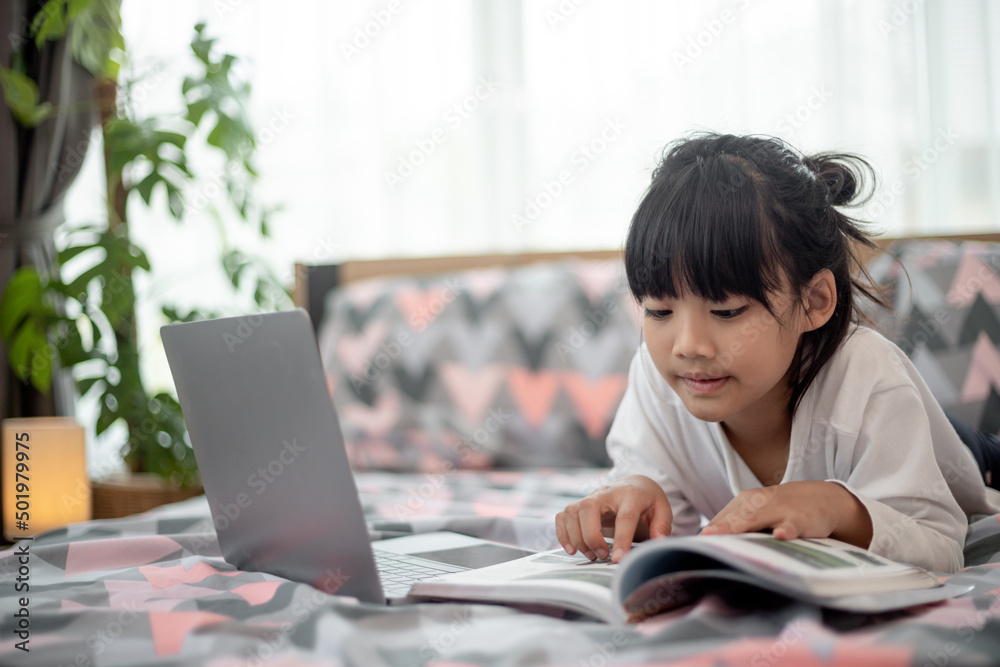 Little Asian girl using a laptop while lying on the bed Little Asian girl using a laptop while lying on the bed